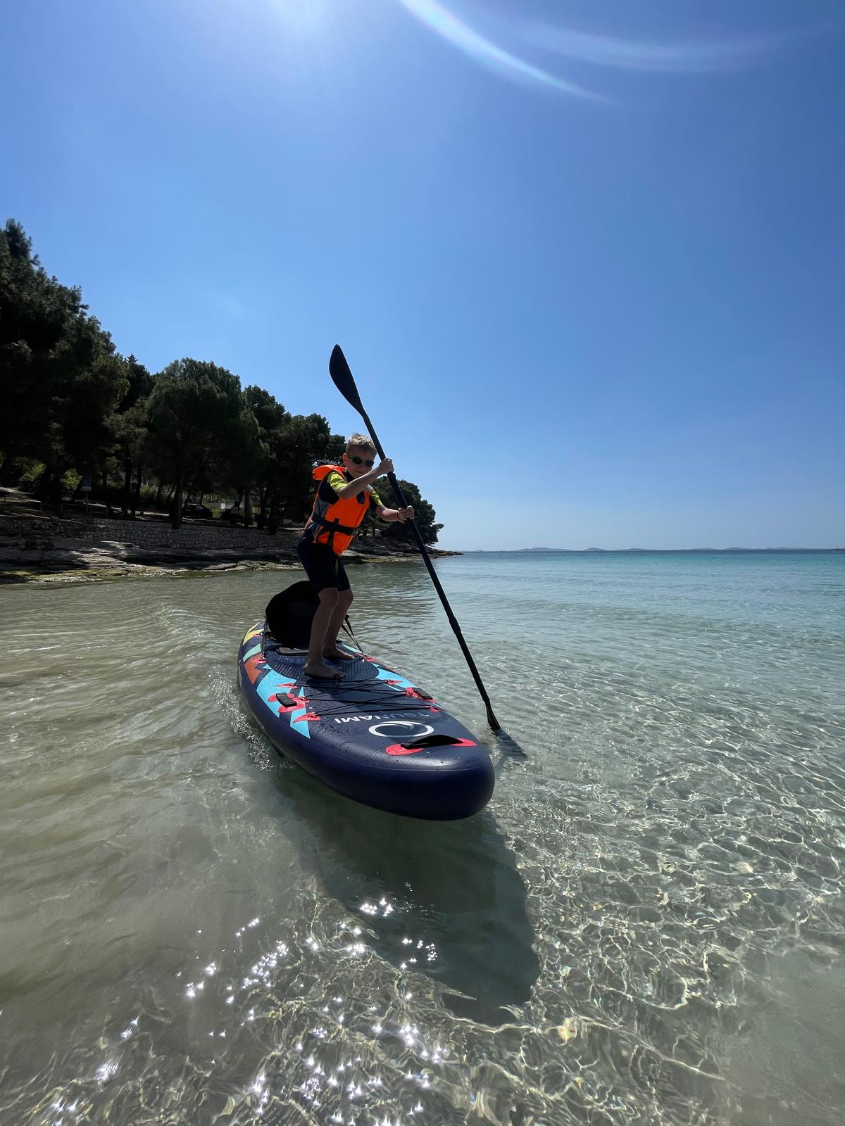 Chłopiec płynący na desce SUP po spokojnej wodzie przy plaży