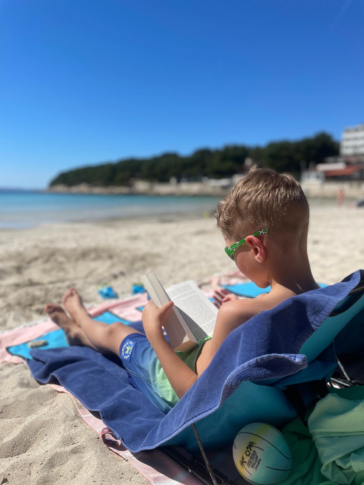 Chłopiec czytający książkę na leżaku przy plaży